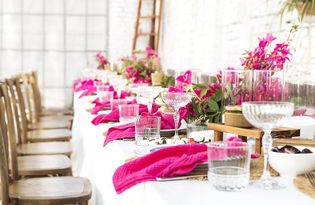A set festive table in the open air. The table is decorated with candles and flowers. Delicious snacks, empty plates, glasses and raspberry napkins. Waiting for the guests