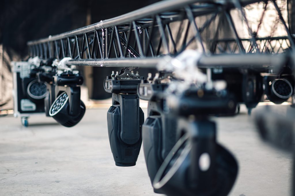 Several moving head spotlights are hanging on a truss system, prepared for an event. The lighting fixtures are waiting to be turned on
